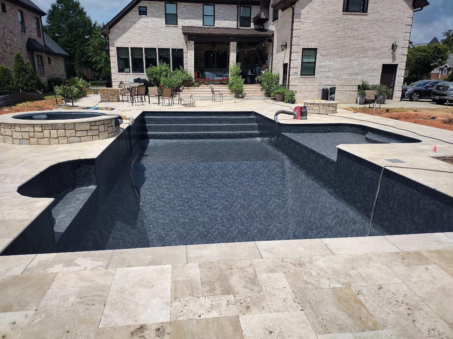 Dark vinyl liner pool with spa and travertine deck