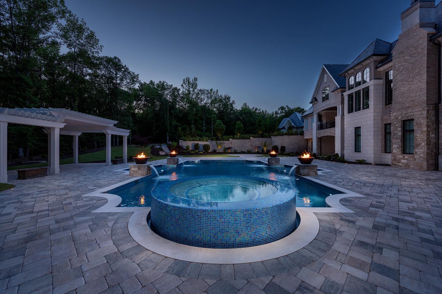 Luxury gunite pool at dusk with fire bowls and mosaic spa